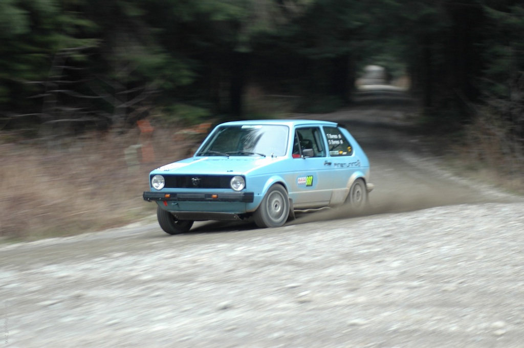 a blue volkswagen rabbit spits up gravel on a rally stage