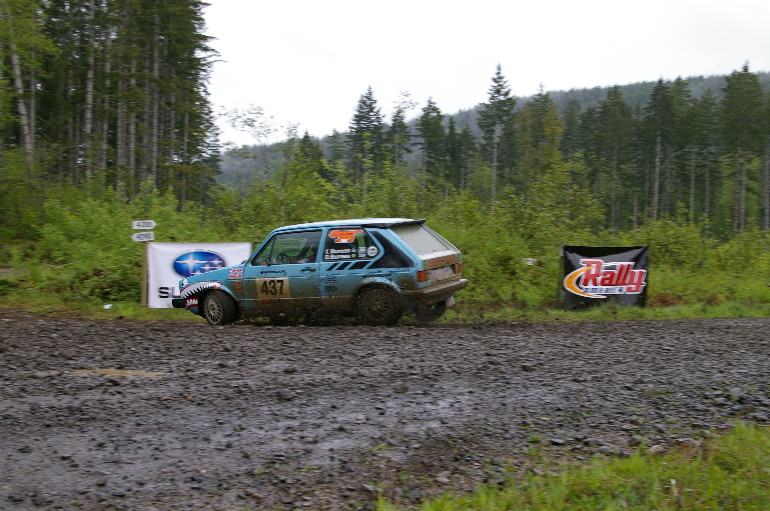 a blue volkswagen rabbit slides around a corner in front of a sponsorship banner