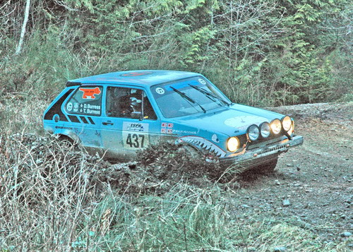 a blue volkswagen rabbit digs into some deep gravel on a rainy rally stage