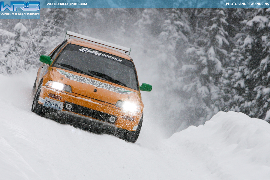 an orange honda civic crests a snowy hill in a winter rally