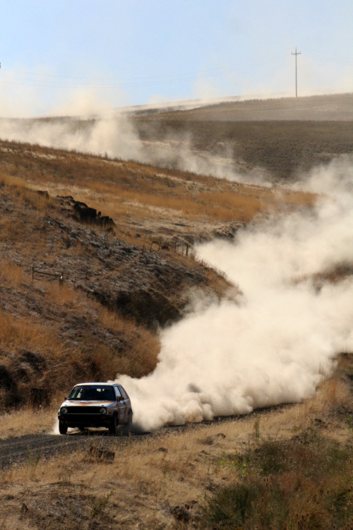 a volkswagen gti with a long trail of dust behind it on a rally stage