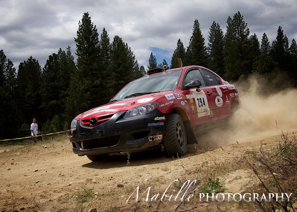 a red mazda 3 slides past the camera on a gravel road