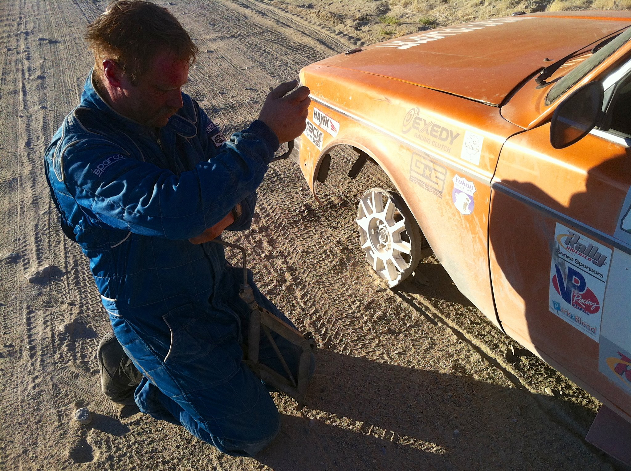 a rally driver works on changing a broken wheel