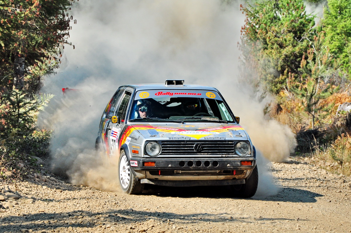 a volkswagen gti emerges from a cloud of dust at the end of a rally stage