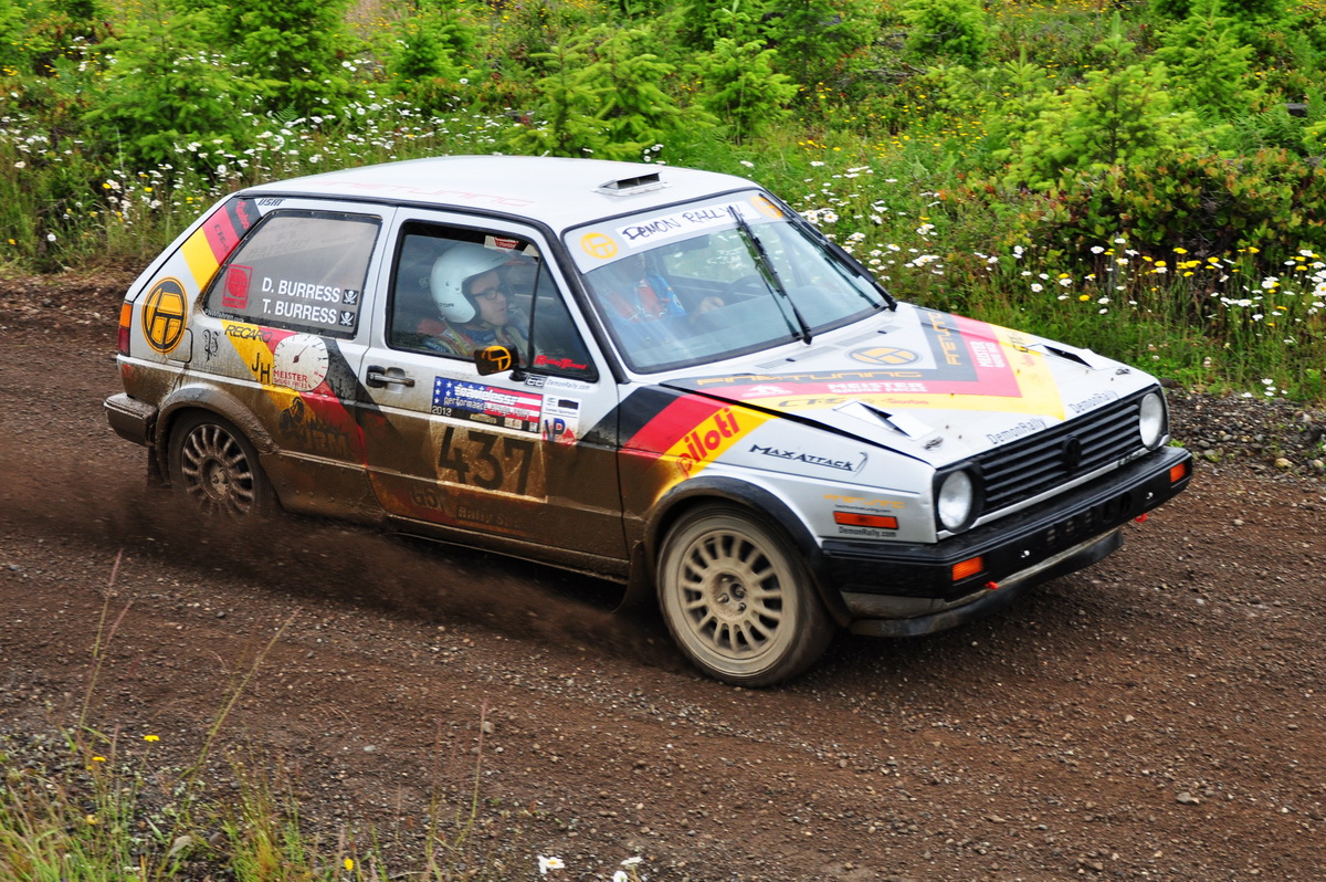 a muddy volkswagen gti zooming past the camera on a gravel road