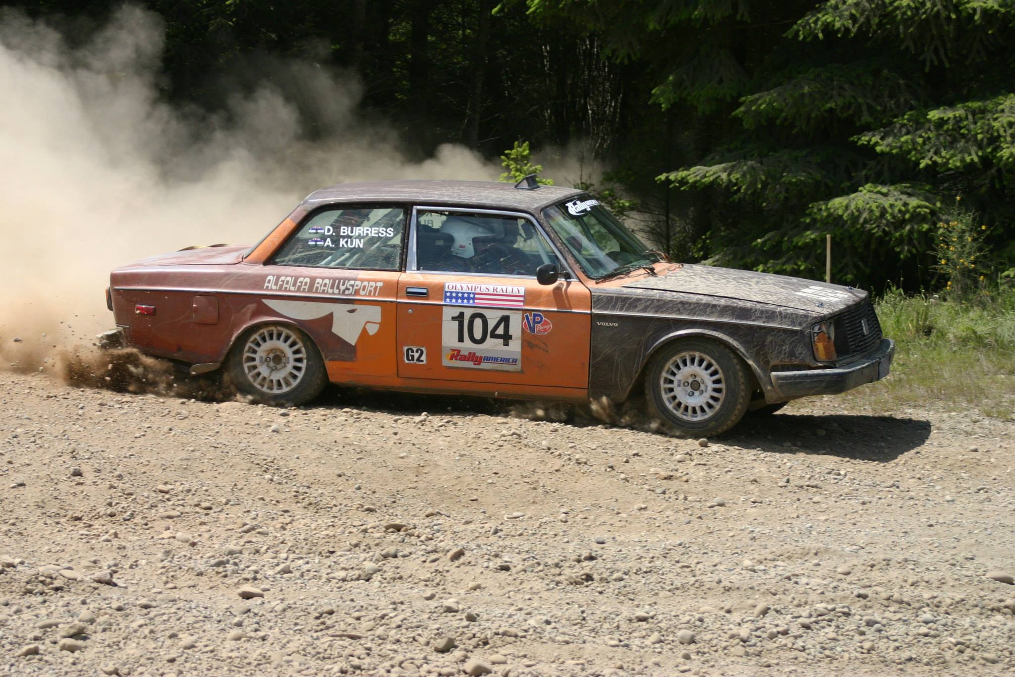 an orange volvo kicking up dust on a wide gravel road