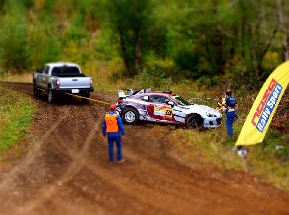 subaru brz race car getting hauled out of the ditch by a mid-zed truck while officials and the driver look on