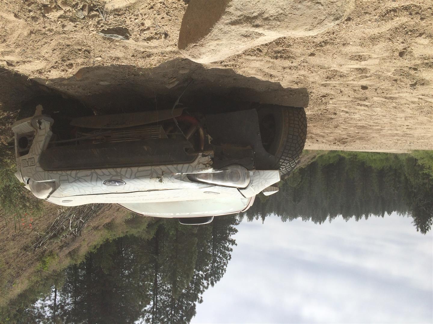 a subaru brz race car with one wheel partially ripped off by a big rock that lies in the middle of the road