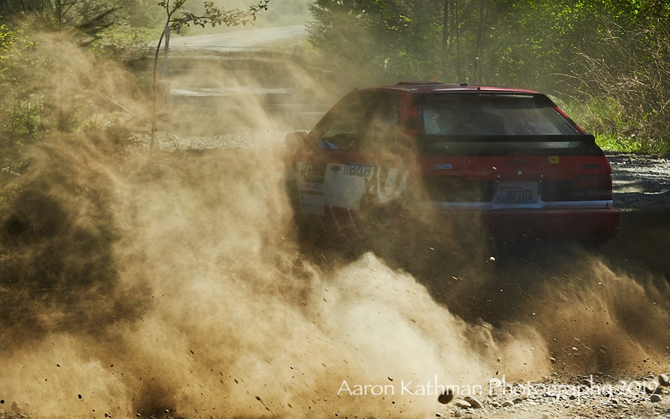 a mazda 323 disappearing into the dust of a rally stage